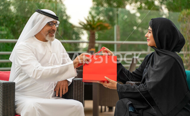 احترام وبر وتقدير الوالدين، الإستمتاع بأجواء عائلية سعيدة في الخارج، صورة مقربة لسيدة سعودية محجبة تقوم بتقديم هدية لوالدها بمناسبة عيد الأب، عائلة عربية خليجية اماراتيه تقضي أوقات ممتعه في أحد المزارع،  مفهوم صلة الرحم.