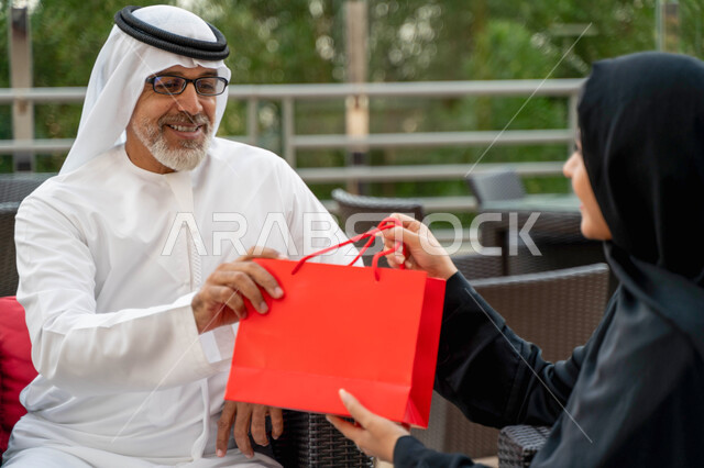 Honoring and respecting parents, enjoying a happy family atmosphere abroad, a close-up of a veiled Saudi woman presenting a gift to her father on the occasion of Father's Day, an Emirati Arab family spending fun times on a farm, the concept of kinship.