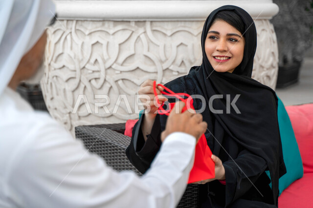 Enjoying a happy family atmosphere outside, a close-up of a veiled Saudi woman presenting a gift to her father on the occasion of Father's Day, an Emirati Arab family spending fun times on a farm, the concept of kinship, honoring, respecting and appreciat