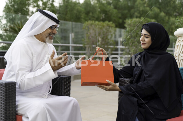  قضاء أوقات ممتعه في أحد المزارع، صورة مقربة لرجل مسن عربي اماراتي يرتدي الكندورة والغترة بايماءات تدل على الفرح والاندهاش، سيدة سعودية تقوم بتقديم هدية لوالدها بمناسبة عيد الأب، الاستمتاع بأجواء عائلية سعيدة في الخارج، مفهوم صلة الرحم. 