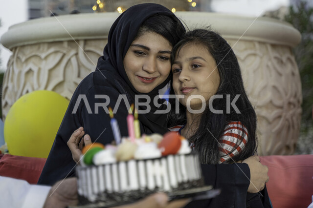 الاحتفال بالذكرى السنوية لولادة الابنه، إيماءات تدل على الفرح والسعادة بالحصول على كعكة يوم الميلاد المزينة بالشموع الملونة، عائلة عربية خليجية إماراتية يحتفلون بعيد ميلاد ابنتهم في الخارج، صورة مقربة لأم سعودية تضم ابنتها بحنان في إحدى المنتزهات