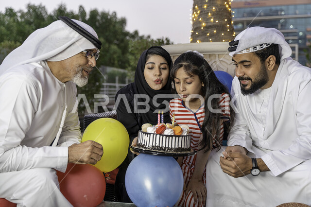 زينة وبالونات الحفلات، ايماءات الود والسرور باجتماع العائلة, صورة مقربة لعائلة عربية خليجية إماراتية تقوم بالاحتفال بعيد الميلاد بأجواء عائلية سعيدة, أسرة سعودية تستمتع بإطفاء شموع الميلاد برفقة الجد في إحدى المنتزهات