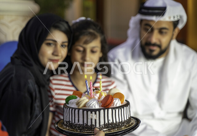 الاحتفال بالمناسبات والأعياد بأجواء عائلية سعيدة, ايماءات السرور والفرح باجتماع العائلة, أسرة عربية خليجية إماراتية تقوم بالاحتفال بعيد الميلاد, فتاة سعودية تستمتع بعيد ميلادها باحتفال عائلي بسيط, تقديم قالب الكيك المزين بالشموع وقضاء أوقات ممتعة مع الأهل