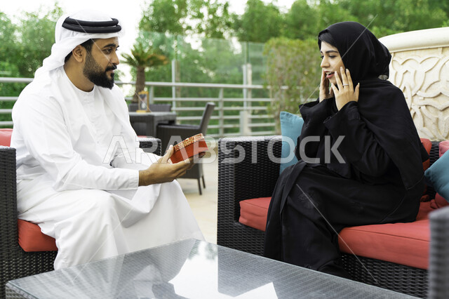 مفهوم الألفة والمحبة بين الزوجين, ايماءات تدل على الدهشة والسرور, مشاركة وتقديم الهدايا في الأعياد والمناسبات العائلية, رجل عربي خليجي إماراتي يقدم لزوجته هدية بمناسبة ذكرى يوم الزواج, رجل وإمرأة سعوديان يحتفلان بعيد الحب في إحدى المنتجعات الفاخرة