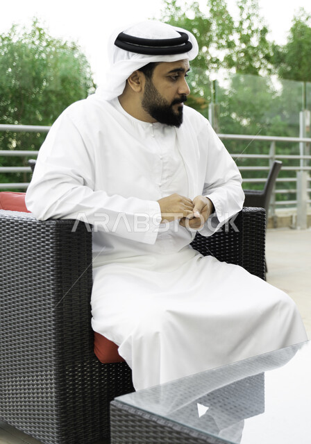 الإستمتاع في الأجواء الهادئه, إيماءات النظر إلى شيء ما, رجل عربي خليجي إماراتي يرتدي الغتره والكندوره الاماراتيه, رجل سعودي يجلس بمفرده في إحدى الجلسات الخارجيه لاحدى المقاهي والمطاعم الفاخره, قضاء أوقات ممتعة في الهواء الطلق.