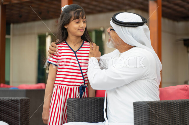 أجواء ممتعة في الهواء الطلق, إكرام وإحترام الأجداد وكبار السن, صورة مقربة لرجل مسن عربي خليجي إماراتي ينظر إلى حفيدته بحب, فتاة سعودية وجدها في جلسه خارجيه راقية, التسامر والضحك مع الأحفاد, الزيارات العائلية ومفهوم صلة الرحم.