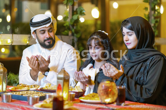 مائدة طعام مليئة بأصناف من المأكولات والمقبلات الشهية، اسلاميات وعبادات رمضانية, عائلة عربية خليجية إماراتية تجلس على سفرة الطعام وتدعو الله عند موعد الإفطار في شهر رمضان المبارك, فضل الدعاء وقت أذان المغرب، أسرة سعودية تستعد لتناول الطعام المطعم 