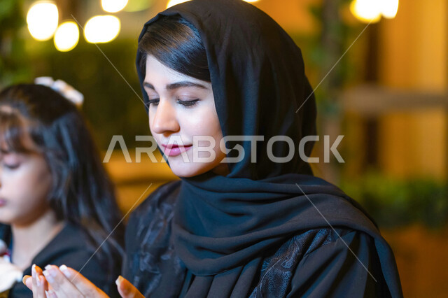  الإستعداد لتناول الطعام في أحدى المطاعم الراقية، أجواء الأسرة السعودية في شهر رمضان، أم عربية خليجية إماراتية مع إبنتها تجلسان على مائدة الطعام وتدعوان الله عند موعد الإفطار, اسلاميات وعبادات رمضانية في الأشهر المباركة