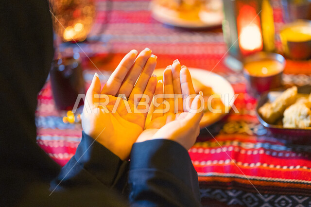  اسلاميات وعبادات رمضانية، شابة سعودية تستعد لتناول الطعام في المطعم، سفرة سحور مليئة بأصناف المأكولات والمقبلات الشهية, صورة مقربة من الخلف لإمرأه عربية خليجية إماراتية تجلس على مائدة الطعام وتدعو الله عند موعد الإفطار في شهر رمضان المبارك