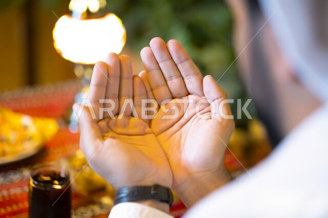 الجلوس على مائدة رمضان وشكر الله بعد تناول الطعام, الدعاء المستجاب وقت أذان المغرب, صورة من الخلف لرجل عربي خليجي إماراتي يستعد للإفطار, رجل سعودي يرفع يديه ويدعو الله تعالى, ايماءات يد تدل على الدعاء والتقرب إلى الله سبحانه وتعالى, إسلاميات وعبادة