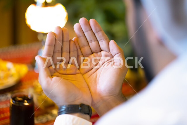 الدعاء المستجاب وقت أذان المغرب, صورة من الخلف لرجل عربي خليجي إماراتي يستعد للإفطار, رجل سعودي يرفع يديه ويدعو الله تعالى, الجلوس على مائدة رمضان وشكر الله بعد تناول الطعام, ايماءات يد تدل على الدعاء والتقرب إلى الله سبحانه وتعالى, إسلاميات وعبادة