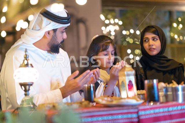اسلاميات وعبادة, أجواء عائلية دينية على مائدة إفطار مليئة بأصناف من المأكولات والمقبلات الشهية, صورة مقربة لعائلة عربية خليجية إماراتية تجلس على سفرة الطعام وتدعو الله عند موعد الإفطار في شهر رمضان المبارك, عائلة سعودية تشكر الله بعد تناول طعام الغداء