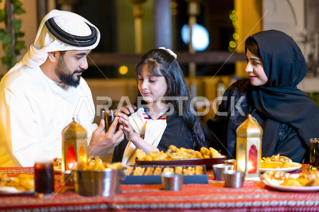 اجتماع الأهل ومشاركة الطعام على مائدة سحور مليئة بأصناف من المأكولات والمقبلات الشهية, صورة مقربة لعائلة عربية خليجية إماراتية تجلس على سفرة إفطار رمضان، أسرة سعودية تستمتع بتناول الفطور الرمضاني خارج المنزل, أجواء عائلية دينية
