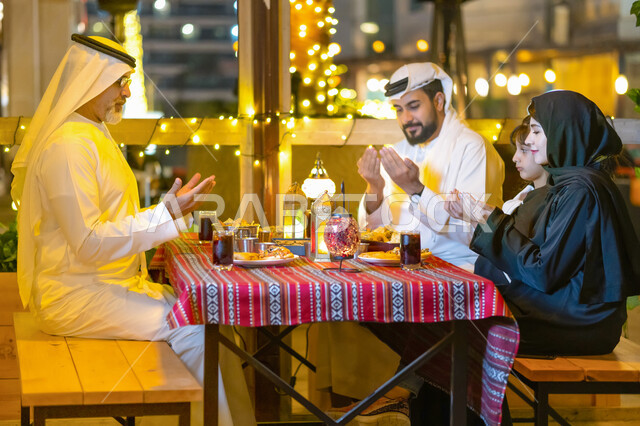 مائدة إفطار مليئة بأصناف المأكولات الشهية، أجواء وعبادات دينية إسلامية، فطور رمضاني عائلي, عائلة عربية خليجية إماراتية تجلس على سفرة الطعام وتدعو الله عند موعد الإفطار في شهر رمضان المبارك, أسرة سعودية تجتمع في إحدى المطاعم المزينة بديكورات رمضانية