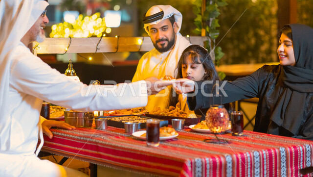 إفطار الصائم عند أذان المغرب, مائدة مليئة بأصناف من المأكولات والمقبلات الشهية, عائلة عربية خليجية إماراتية مستمتعة بتناول السحور في شهر رمضان المبارك, أسرة سعودية تجلس في مطعم مزين بديكورات رمضانيه, مشاركة الطعام وإكرام الآخرين