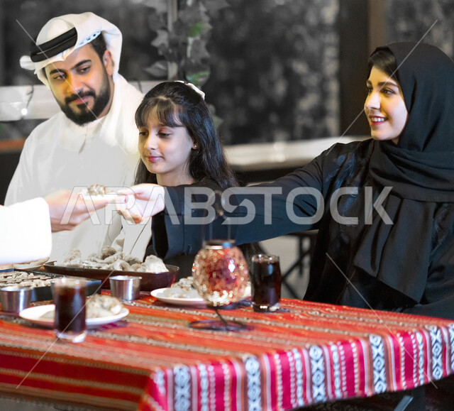 مشاركة الطعام وإكرام الآخرين, ايماءات وجه تدل على السعادة بقضاء أوقات عائلية ممتعة, احترام الوالدين والأهل والأقارب, صورة مقربة لعائلة عربية خليجية إماراتية تجلس على مائدة إفطار رمضان, أسرة سعودية تستمتع بتناول السحور الرمضاني خارج المنزل