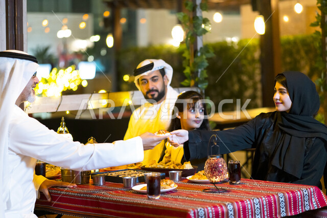إجتماع الأهل على مائدة السحور, مشاركة الطعام وإكرام الوالدين, سفرة إفطار مليئة بأصناف من المأكولات والمقبلات الشهية, عائلة عربية خليجية إماراتية مستمتعة بتناول الفطور في شهر رمضان, أسره سعودية تجلس في مطعم مزين بديكورات رمضانيه, أجواء عائلية رمضانية.