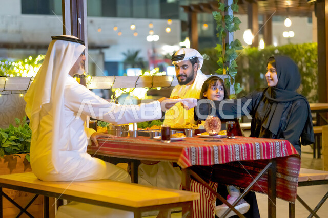 سفرة إفطار مليئة بأصناف من المأكولات والمقبلات الشهية, عائلة عربية خليجية إماراتية مستمتعة بتناول الفطور في شهر رمضان, أسره سعودية تجلس في مطعم مزين بديكورات رمضانيه, إجتماع الأهل على مائدة السحور, مشاركة الطعام وإكرام الوالدين, أجواء عائلية رمضانية.