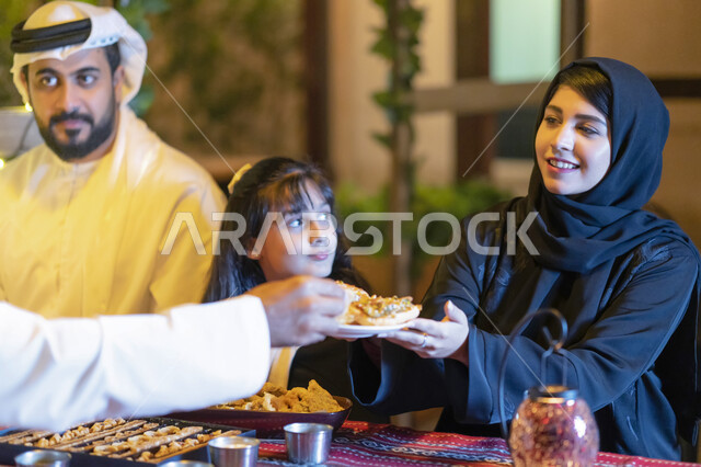 مائدة إفطار مليئة بأصناف من المأكولات والمقبلات الشهية, صورة مقربة لعائلة عربية خليجية إماراتية مستمتعة بتناول الفطور في شهر رمضان المبارك, أسره سعودية تجلس في مطعم مزين بديكورات رمضانيه, إجتماع الأهل على مائدة السحور, مشاركة الطعام وإكرام الضيف. 
