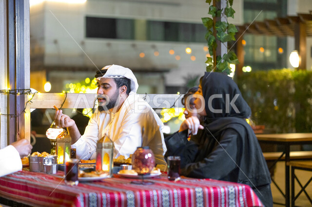 سفرة سحور مليئة بأصناف من المأكولات والمقبلات الشهية, عائلة عربية خليجية إماراتية مستمتعة بتناول الطعام في شهر رمضان المبارك, أسره سعودية تجلس في مطعم مزين بديكورات رمضانيه, أجواء عائلية رمضانيه, إجتماع الأهل على مائدة الإفطار. 