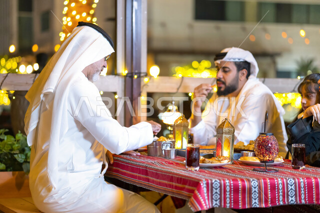 An Iftar meal filled with varieties of delicious food and appetizers, an Emirati Arab family enjoying eating in the blessed month of Ramadan, a Saudi family sitting in a restaurant decorated with Ramadan decorations, a Ramadan family atmosphere, the famil