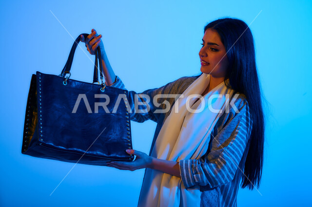 بورتريه لإمرأه عربية سعوديه خليجية ترتدي عباءه ملونه أنيقه، تحمل بيدها حقيبة جلد كبيره, شراء الحقائب, عارضة أزياء، ملابس نسائية بتصاميم عصرية مميزة، الجمال والاناقة، منتجات نسائيه سعوديه، التسوق والشراء, موديلات خليجية, أزياء وإكسسوارات, متابعة الأزياء وا
