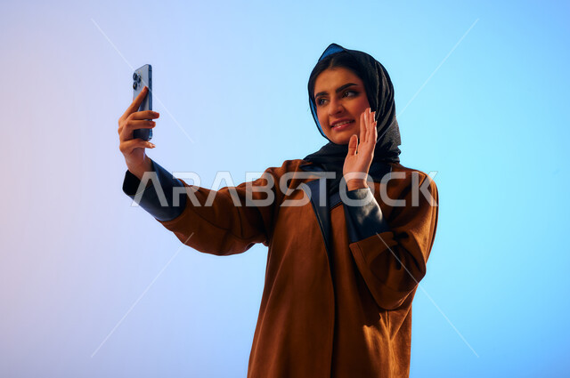 Portrait of a Saudi Arab Gulf woman, holding a mobile phone in her hand, making a video call, taking a selfie, taking souvenir photos, social media, acquaintance and friendships, smiling face gestures, the concept of using technology devices and modern te