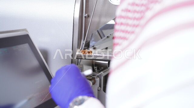 صورة مقربة لرجل عربي خليجي سعودي يقوم بإستخدام ماكينة تعمل على تحميص حبوب البن ، حماصة القهوة ، آلة تحميص القهوة ، مطاحن القهوة ، محمصة سعودية ، مشاريع إنتاجية سعودية ، مصانع إنتاج سعودي ، صناعات غذائية