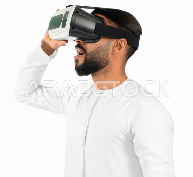 الإستمتاع بمشاهدة الأفلام و محاكاة العالم الإفتراضي، بورتريه لرجل إماراتي عربي خليجي يرتدي الكندورة الإماراتية ونظارات الواقع الإفتراضي (في آر) ثلاثية الإبعاد، إيماءات وجه تدل على الدهشة والتعجب والإستغراب، خلفية بيضاء