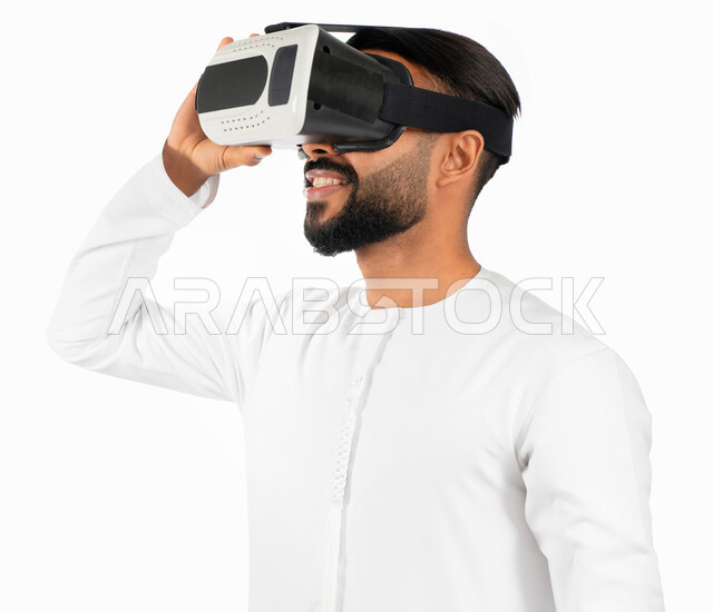 إيماءات تدل على السعادة والمتعة، بورتريه لرجل إماراتي عربي خليجي يرتدي الكندورة الإماراتية ونظارات الواقع الإفتراضي (في آر) ثلاثية الإبعاد، الإستمتاع بمشاهدة الأفلام و محاكاة العالم الإفتراضي، خلفية بيضاء