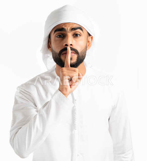 الهدوء والسكون وعدم الإزعاج، بورتريه لرجل عربي خليجي إماراتي يرتدي العمامة والكندورة الإماراتية ويضع أصبع السبابة على فمه، التوقف عن الكلام وخفض الصوت، إيماءات وجه ويدين تدل على طلب السكوت والصمت، حركة أصبع وإشارات، خلفية بيضاء