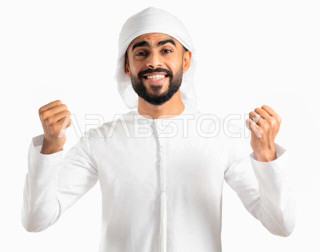 النجاح والقوة وتحقيق الاهداف، إيماءات يدين تدل على الحماس والشغف، بورتريه لرجل عربي خليجي إماراتي يرتدي العمامة والكندورة الإماراتية، المنافسة والتحدي والتشجيع، الفرح والسعادة بالفوز والإنتصار، خلفية بيضاء