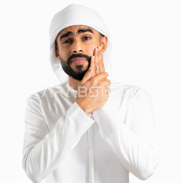 Gingivitis and tooth decay, a portrait of a Gulf Arab Emirati man wearing a turban and an Emirati kandora and placing his hand on his face. Face and hand gestures indicate pain and mouth pain, fatigue, exhaustion and swollen mouth, the need to visit the d