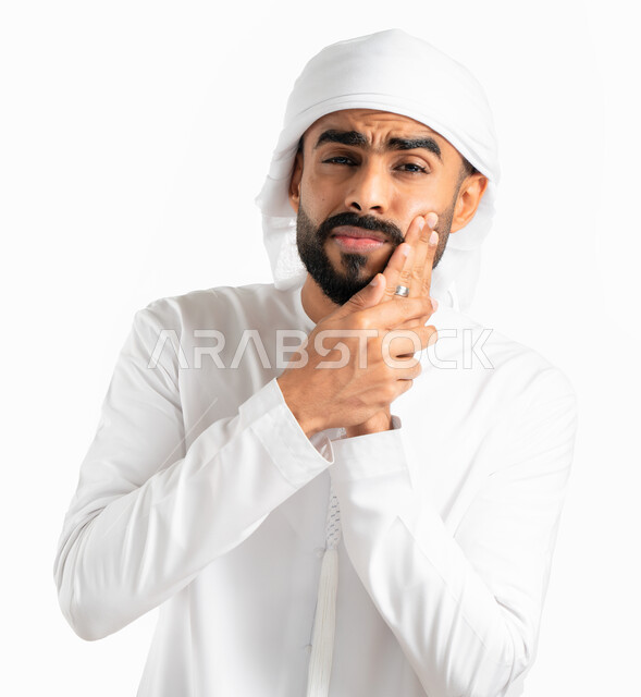 التعب والإرهاق وإنتفاخ الفم، بورتريه لرجل عربي خليجي إماراتي يرتدي العمامة والكندورة الإماراتية ويضع يده على وجهه، إيماءات وجه ويدين تدل على الألم ووجع الفم، إلتهاب اللثة وتسوس الأسنان، الحاجة لزيارة طبيب الأسنان، خلفية بيضاء