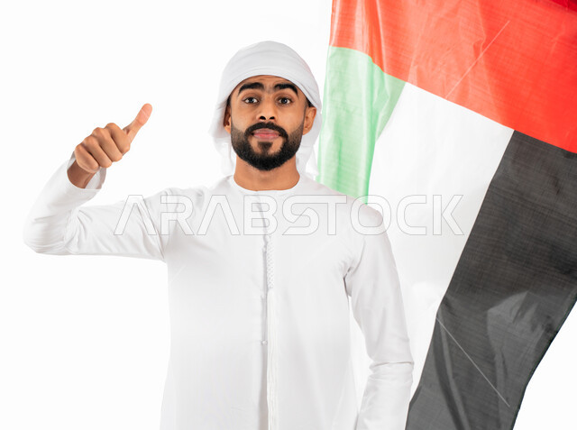 إيماءات الإعجاب والقبول والرضى، بورتريه لرجل عربي خليجي إماراتي يرتدي العمامة والكندورة الإماراتية ويرفع أصبع الإبهام لأعلى، إحياء ذكرى إستقلال الإمارات، الإحتفال بالعيد الوطني الإماراتي، علم دولة الإمارات العربية المتحدة، حب الوطن والعلم، خلفية بيضاء