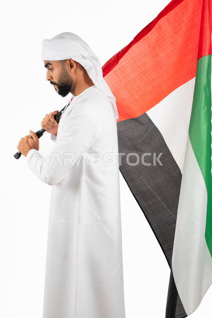 إحياء ذكرى الإستقلال لدولة الإمارات العربية المتحدة، بورتريه من الجانب لرجل عربي خليجي إماراتي يرتدي العمامة والكندورة الإماراتية يحمل علم الإمارات، الإحتفال بالعيد الوطني الإماراتي، حب الوطن والعلم، خلفية بيضاء
