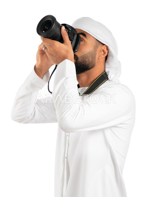 إلتقاط الصور الفوتوغرافية بإستخدام كاميرا التصوير عالية الدقة، بورتريه لمصور إماراتي خليجي عربي يرتدي الكندورة والعمامة الإماراتية ويوجه الكاميرا لأعلى، احتراف فن التصوير، خلفية بيضاء 