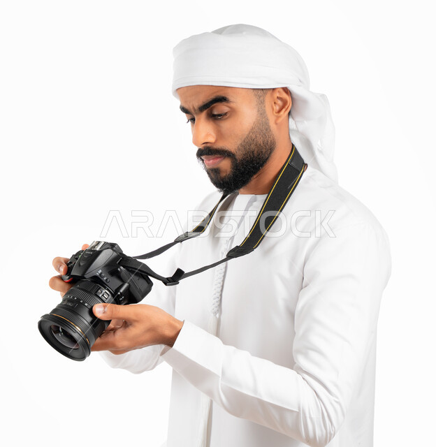 مراجعة وفحص وإختيار الصور، بورتريه لمصور خليجي عربي إماراتي يرتدي الكندورة والعمامة الإماراتية ويقوم بإلتقاط الصور الفوتوغرافية بإستخدام كاميرا التصوير عالية الدقة، احتراف فن التصوير، خلفية بيضاء