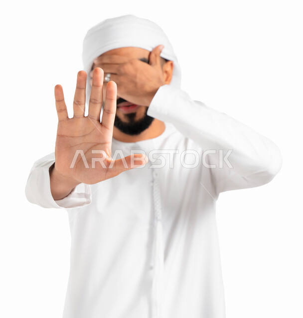 إيماءات الخوف والقلق والانزعاج من أمر ما، عدم القبول ورفض الأذى، بورتريه لرجل عربي خليجي إماراتي يرتدي الكندورة والعمامة الإماراتية ويقوم بتغطية عينه ورفع يده الأخرى لأعلى بإشارة توقف، طلب التوقف والإمتناع عن فعل شيء ما، خلفية بيضاء