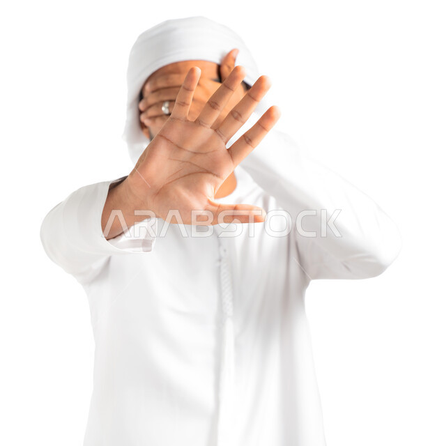 طلب التوقف والإمتناع عن فعل شيء ما، بورتريه لرجل عربي خليجي إماراتي يرتدي الكندورة والعمامة الإماراتية ويقوم بتغطية عينه ورفع يده الأخرى لأعلى بإشارة توقف، إيماءات الخوف والقلق والانزعاج من أمر ما، عدم القبول ورفض الأذى، خلفية بيضاء