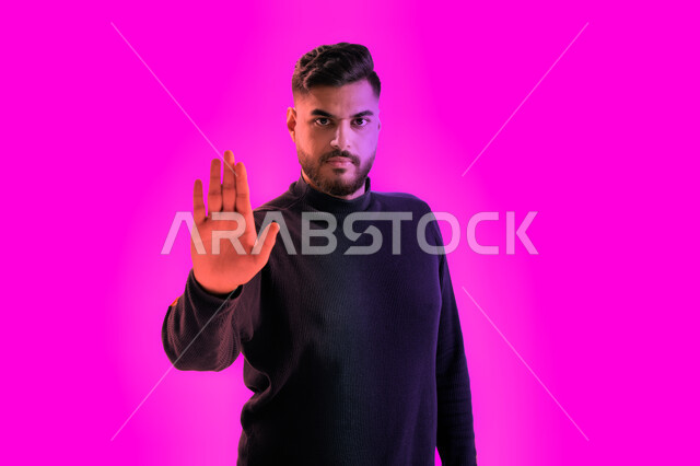 إيماءات وجه غاضبة ويدين تدل على المنع والتوقف عن فعل شيء ما، بورتريه مقرب لشاب سعودي يقوم بجلسة تصوير يرتدي الزي الكاجوال، الشعور بالخوف و الإنزعاج, رجل عربي خليجي إماراتي يعبر عن الرفض والإمتناع وايقاف أمر ما، خلفية ملونة