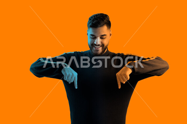 تأكيد حدوث شيء هذه اللحظة، بورتريه مقرب لرجل سعودي يرتدي الزي الكاجوال, يؤشر بيديه للأسفل الى شيء ما, حركات تدل على المكان، رجل عربي خليجي إماراتي مبتسم وسعيد يشير لشيء ما، خلفية ملونة 