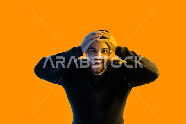 ايماءات وجه ويدين تدل على الحماس والسعادة، بورتريه مقرب لرجل عربي إماراتي خليجي مبتسم يضع يديه على رأسه ينظر إلى الكاميرا، مفهوم الأناقة والموضة، رجل سعودي يرتدي الزي الكاجوال، التشوق والرغبة لفعل شيء ما، خلفية ملونة