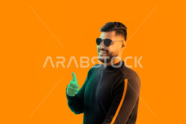 Hand gestures indicating approval, acceptance and satisfaction, a close-up portrait of an Emirati Arab man raising his thumb up, a young Saudi man wearing casual attire and sunglasses, privilege, distinction and success, yellow background