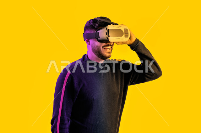 التفاعل مع الفيلم ومحاكاة العالم الخيالي، رجل سعودي مبتسم يقوم بمشاهدة أفلام عبر نظارات الواقع الإفتراضي، بورتريه جانبي مقرب لشاب عربي اماراتي خليجي يرتدي الزي الكاجوال ونظارة الواقع الافتراضي ثلاثية الأبعاد, ايماءات تدل على السعادة والمتعة, خلفية صفراء
