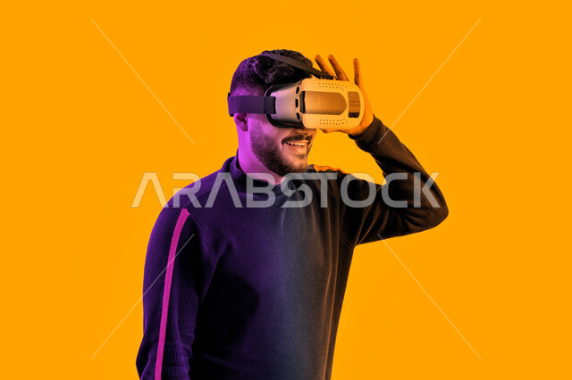 التفاعل مع الفيلم ومحاكاة العالم الخيالي، رجل سعودي مبتسم يقوم بمشاهدة أفلام عبر نظارات الواقع الإفتراضي، بورتريه جانبي مقرب لشاب عربي اماراتي خليجي يرتدي الزي الكاجوال ونظارة الواقع الافتراضي ثلاثية الأبعاد, ايماءات تدل على السعادة والمتعة, خلفية صفراء