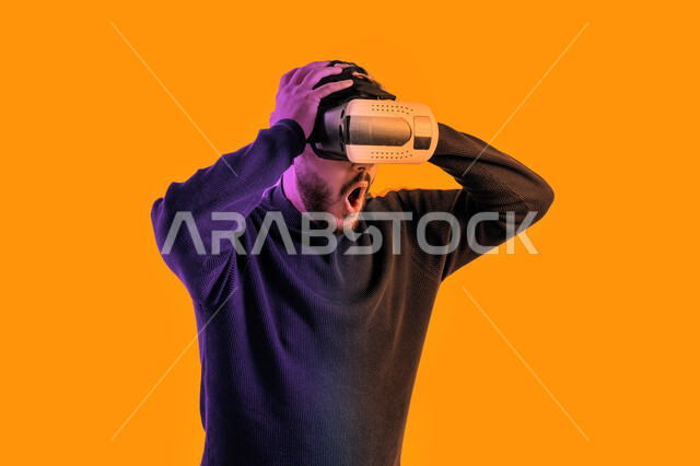Face and hand gestures indicating astonishment and astonishment, an Emirati young man watching movies through virtual reality glasses, a close-up portrait of a Saudi Arabian Gulf man wearing casual clothes and 3D virtual reality glasses, interaction with 