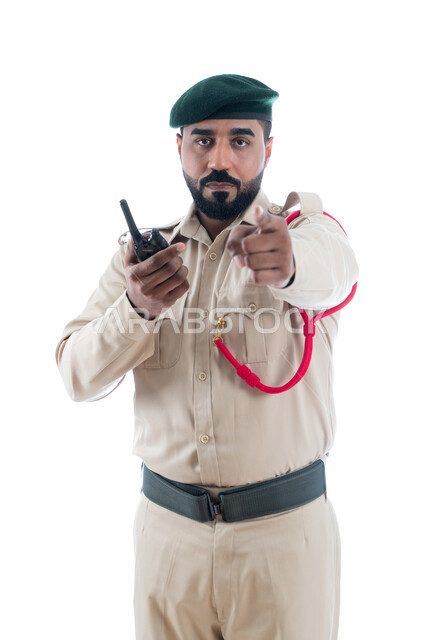 الإشارة بإصبع السبابة نحو شيء ما، الإستجابة لحالات الطوارئ، الحفاظ الأمن والأمان والطمأنينة، بورتريه لشرطي عربي خليجي إماراتي يرتدي الزي العسكري ويستخدم جهاز الإرسال والإستقبال اللاسلكي، حركة إصبع وإشارات، تأمين المنشأت وحماية الأفراد، خلفية بيضاء