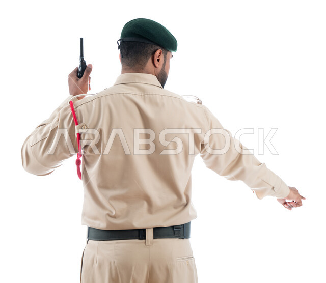 تأمين المنشأت وحماية الأفراد، بورتريه من الخلف لشرطي عربي خليجي إماراتي يستخدم جهاز الإرسال والإستقبال اللاسلكي ويرتدي الزي العسكري ويشير بإصبع السبابة نحو شيء ما، حركة إصبع وإشارات، الحفاظ الأمن والأمان والطمأنينة، تعزيز الثقة بالشرطة، خلفية بيضاء