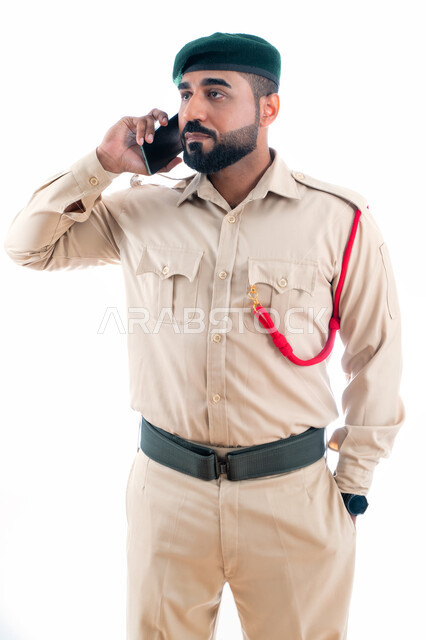 اجراء مكالمة من خلال الجوال، الإستجابة لحالات الطوارئ، التواصل مع الأفراد، بورتريه لشرطي عربي إماراتي خليجي يرتدي بدلة الشرطة ويستخدم الهاتف المحمول، إدارة الأزمات والكوراث، تعزيز الأمن والأمان والثقة بالشرطة، خلفية بيضاء